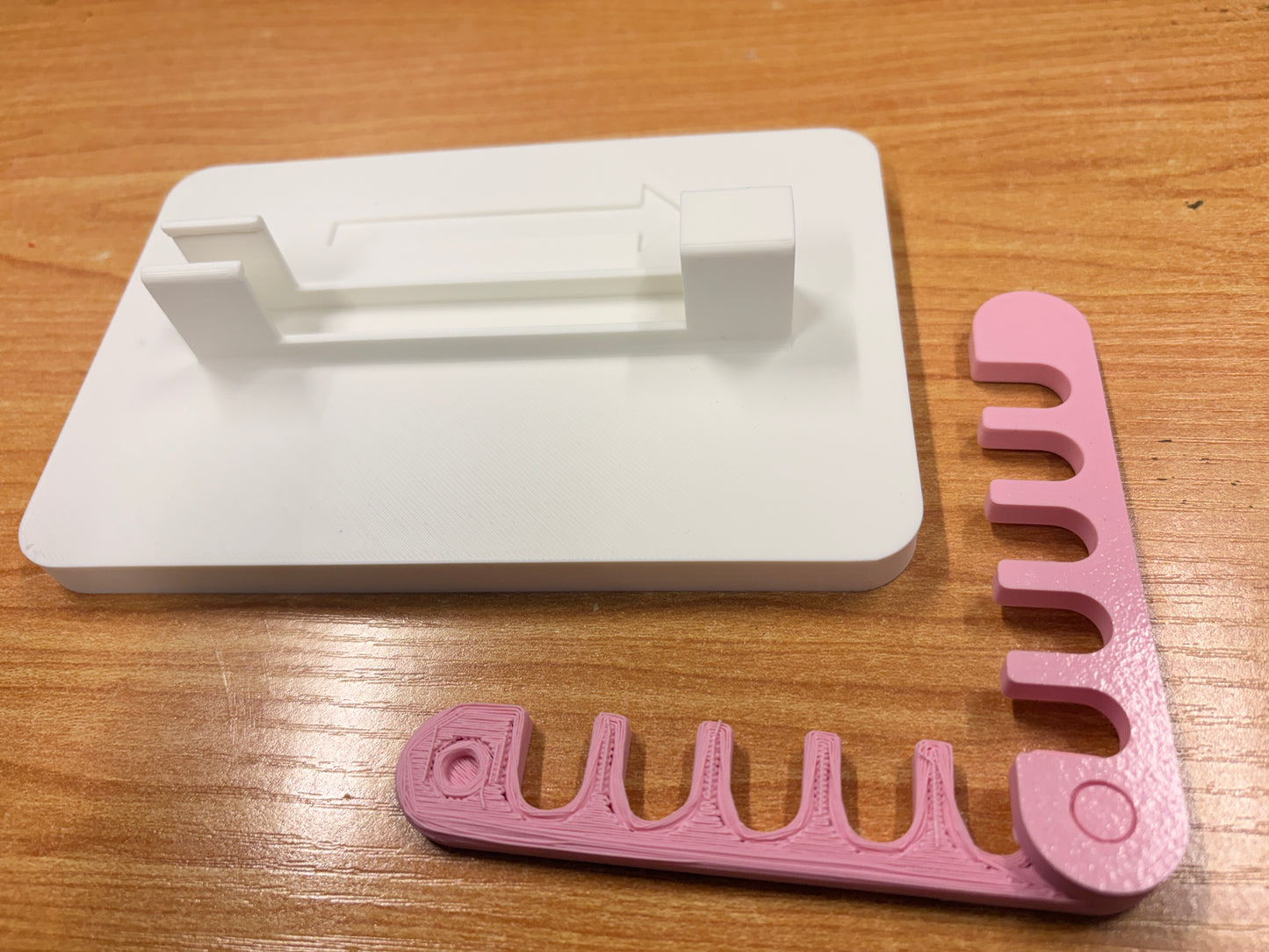 A pink plastic yarn guide with five curved slots, resting on a white plastic storage tray over a wooden tabletop.